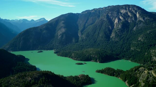 Aerial drone cinematic wide view of emerald green diablo lake surrounded by dramatic mountain ranges and forested alpine landscape in north cascades national park, washington