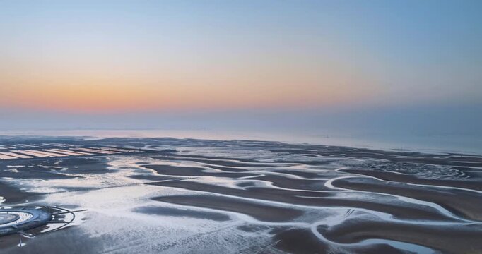 Aerial time-lapse of the Yellow Sea mudflats at dawn, capturing serene natural patterns and soft golden light over tidal flats in Rizhao, Shandong Province, China
