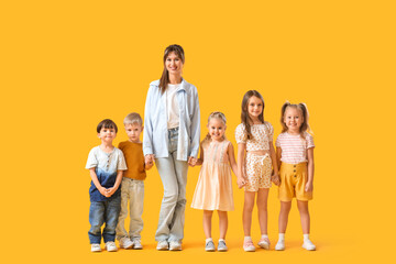 Group of little children with nursery teacher holding hands on yellow background