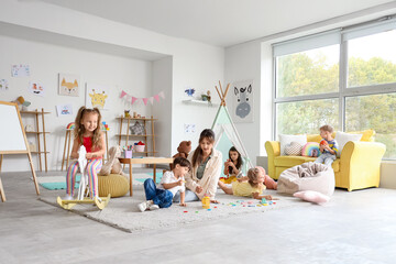 Group of cute little children with nursery teacher playing in kindergarten