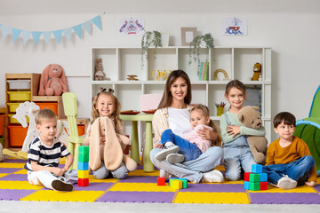 Group of little children with toys and nursery teacher sitting in kindergarten