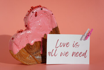 LOVE IS ALL WE NEED message on paper note greeting card Delicious fresh croissant topped with colorful flavor Ganache. Creation unique heart shape bakery. Puff pastry holiday love gift present idea