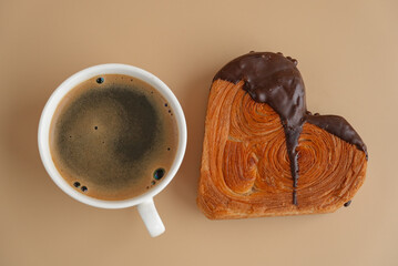 Latte cappuccino coffee drink with Delicious fresh croissant topped with Dark chocolate flavor Ganache. Creation unique heart shape bakery. Puff pastry holiday love gift present idea Valentine's day