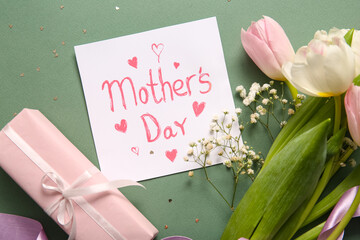 Card with text MOTHER'S DAY, gift box and beautiful flowers on grey background, closeup