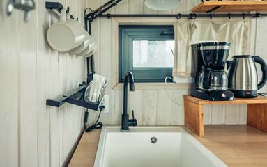 modern kitchen with sleek black faucet and coffee maker. White wooden walls and hanging mugs create a cozy atmosphere