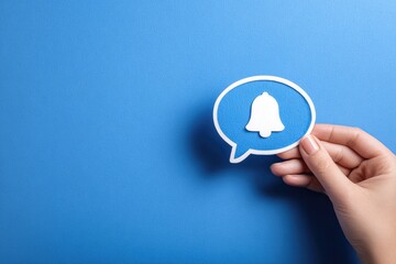 Hand holding a speech bubble with a notification bell, over a blue background