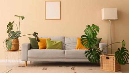 Cozy sofa, lamp and Monstera houseplants in interior of living room