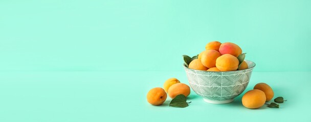 Bowl of tasty ripe apricots on turquoise background with space for text