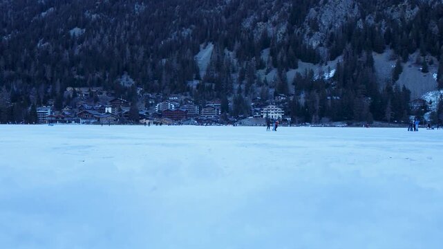 Aerial drone footage of Champex-Lac, Switzerland, showing a frozen alpine lake where people ice skate in winter. Snowy mountains and nature. Filmed in 4K with a DJI Mini 2.
