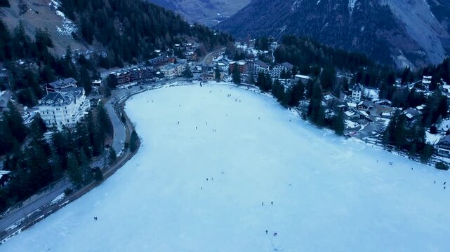 Aerial drone footage of a frozen lake in Champex, Switzerland, with people ice skating in winter. Shot in 4K by a professional drone pilot using a DJI Mini 2.