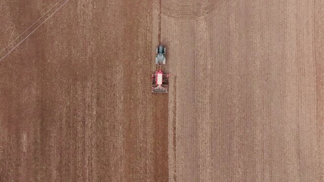 Top view agricultural tractor red seeder planting crops in cultivated brown soil