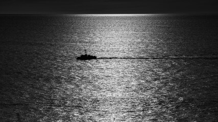Silhouette of a fishing boat crossing a shimmering Pacific horizon in black and white