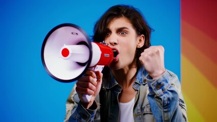 A person shouts intensely into a megaphone, clenched fist raised, with a bright, colorful background