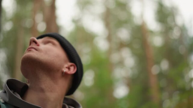 White man hiker birdwatcher looking up at tall pine canopy, peaceful profile shot, beanie and flannel jacket, soft sunlight filtering through trees, contemplative expression, mossy forest floor