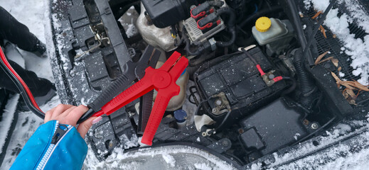 Crocodile clips for starting a car engine with a car in the background with the hood open. Tools to help drivers