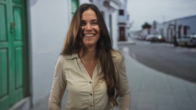 Young hispanic woman making claw hands gesture with visible hands and broad smile on a city street beside a green door; playful mischief.