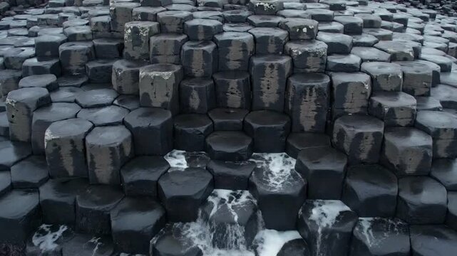 Aerial view of Giant Causeway basalt columns with ocean waves crashing against dark hexagonal rocks in Northern Ireland nature landscape
