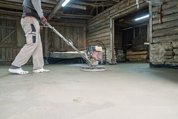 Fototapeta premium A construction worker operates a concrete grinding machine, skillfully smoothing a surface in a rustic building. This process is vital for creating durable and polished concrete floors.