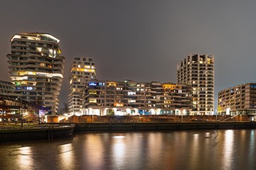 Fototapeta premium Night scene in Hamburg, showcasing modern architecture. Illuminated buildings reflect in the water, capturing the urban vibrancy and design of Hamburg, Germany.