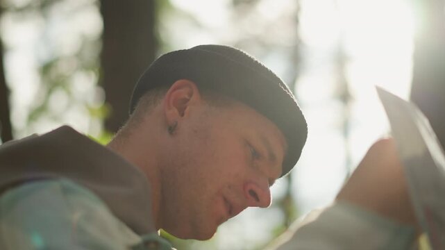 white guide focused on paper map, sunlit portrait among tall pines, concentrated expression, earring glint, hoodie and backpack straps visible, careful waypoint scanning, cinematic backlight creating