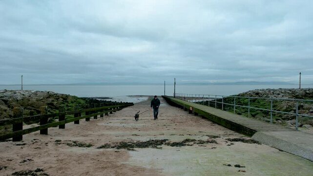 Man walking his lurcher dog along the beach in Morecambe on a grey overcast winter day in December