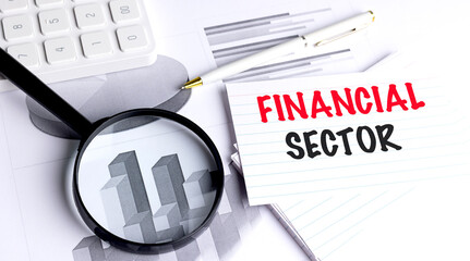 Financial sector phrase on lined index card with magnifying glass, pen, calculator and financial charts