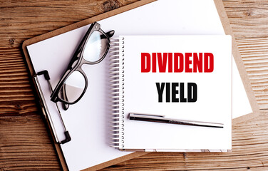 Dividend yield phrase written on spiral notepad with pen and eyeglasses on wooden office desk