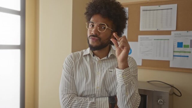 African american man gesturing small size in a modern office with charts and reports on a corkboard behind him.