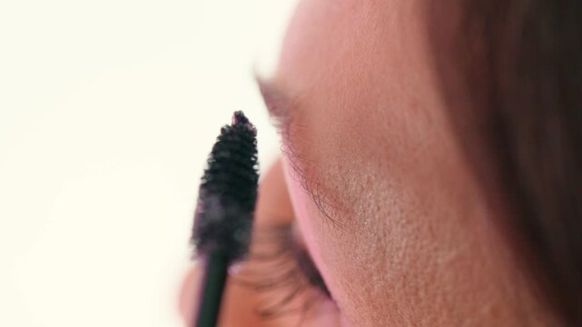 Macro closeup of a beautician applying brow tint with a spoolie brush on a female client in a beauty salon. Focus on eyebrow and skin texture, natural look, clean tools, professional service