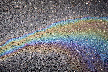 A shiny puddle of gasoline creates stunning iridescent reflections on dark asphalt.