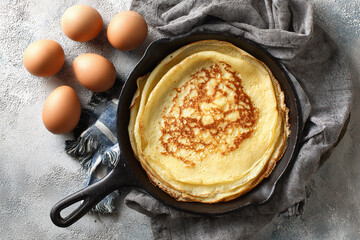 Stack of golden crepes in a cast iron pan with fresh eggs on the side