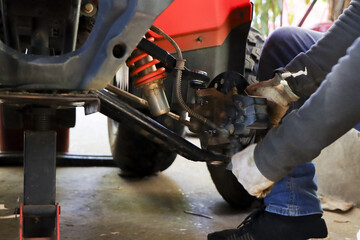 Mechanic performing maintenance on vehicle suspension system with jack stand adjusting shock absorber spring and brake assembly with serious professional focus on repair work