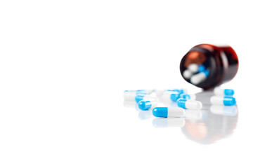 Blue capsules spilled from medicine bottle isolated on white background.