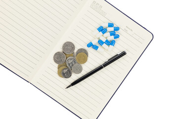 Open notebook with blue capsules and coins isolated on white background with clipping path.