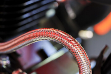 Close up mechanical red braided hose curve over motorcycle engine part presenting powerful textured...