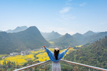 Young happy woman tourist enjoying the canola fields with mountain views while traveling in Luoping, China