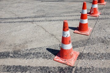Orange traffic cones aligned on damaged asphalt road, marking lane separation and roadwork area, symbolizing safety, caution, infrastructure maintenance, and urban traffic control.