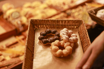 Fototapeta premium Delicious fresh donut rings with sweet glaze and chocolate topping served on wicker tray in bakery shop for tasty dessert or snack by anonymous hand holding food