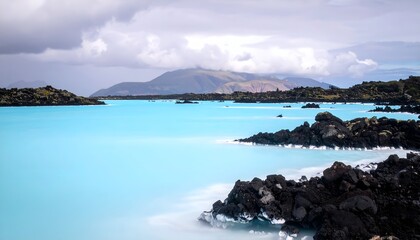 Teal geothermal lagoon with dark rocks and distant mountains under cloudy sky