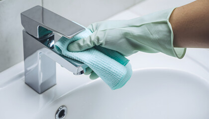 Gloved Hand Cleaning Bathroom Sink Faucet With Cloth