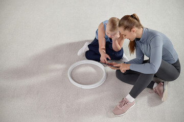 Naklejka premium Caucasian woman sitting on floor with Caucasian child with Down syndrome, both interacting with digital tablet, child appearing engaged while woman guiding and supporting activity