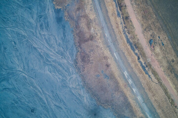 Blue toxic sludge near asphalt road, industrial chemical waste texture, environmental pollution concept, aerial drone shot top view