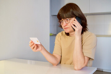 Woman making phone call, holding credit card and showing worried expression