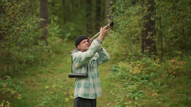 caucasian woodsman signaling with handmade horn on forest path, blowing rustic wooden horn, echoing sound across canopy, plaid jacket and beanie, backpack at side, nostalgic rural mood, solitude
