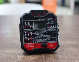 A professional digital socket tester tool on a wooden surface for electrical safety inspections.