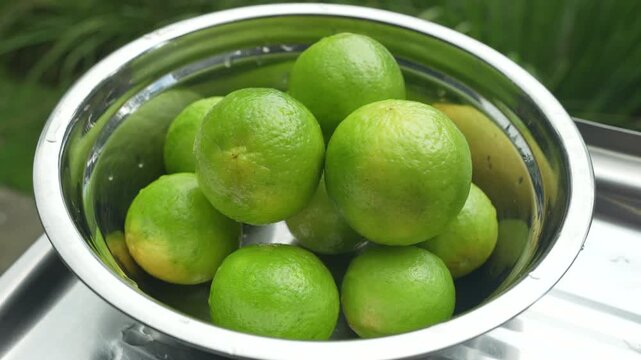 A silver bowl full of green limes ready to make lime juice.