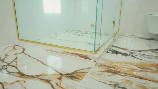 pov a modern glass shower enclosure with gold trim on a polished marble bathroom floor. luxury interior design, clean architecture, and elegant bathroom renovation.