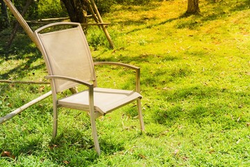 Empty outdoor chair on green grass in a sunny garden, peaceful backyard scene with natural light, relaxation concept and copy space.