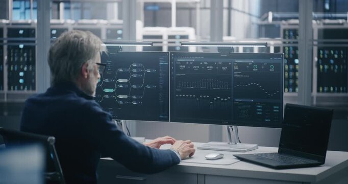 Senior Engineer Monitoring Data Flow on Dual Screens and Laptop. IT Specialist Working on Monitors Displaying Complex Network Diagrams and Analytics in Data Center. Network Security and Monitoring.