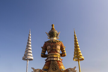 Rear view of a giant guardian statue beside golden and silver ceremonial umbrellas, representing Thai temple art, spirituality, tradition, and cultural heritage